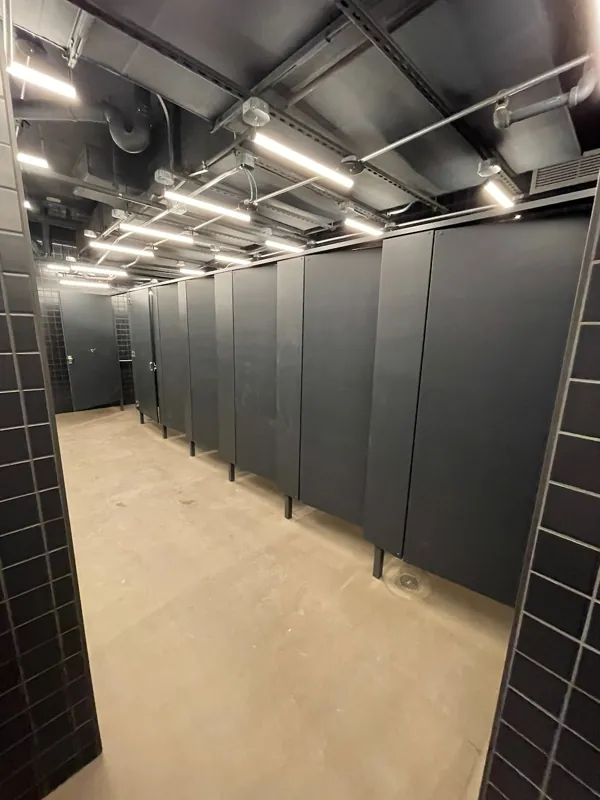 A row of black restroom compartments beneath an exposed ceiling