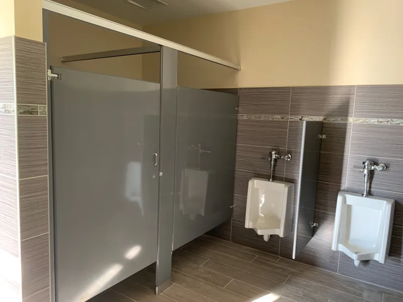 Metal restroom partitions and urinal screens against dark tile