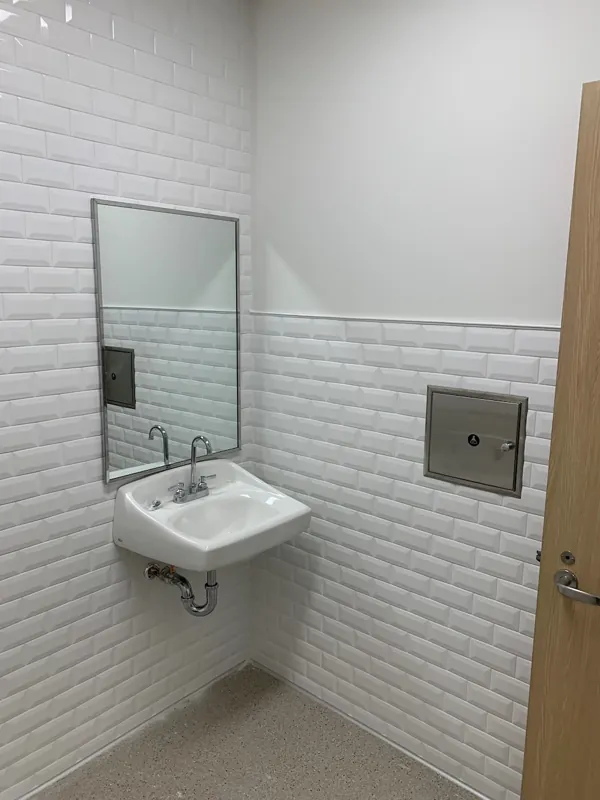 Wall mirror and recessed dispenser beside a restroom sink
