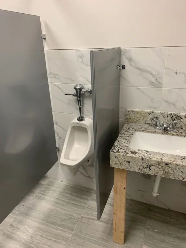 A gray urinal screen in a marble-look tiled restroom