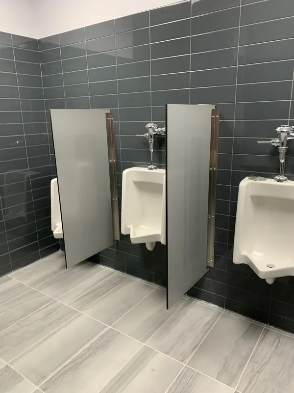 Gray privacy screens installed between urinals against dark tile