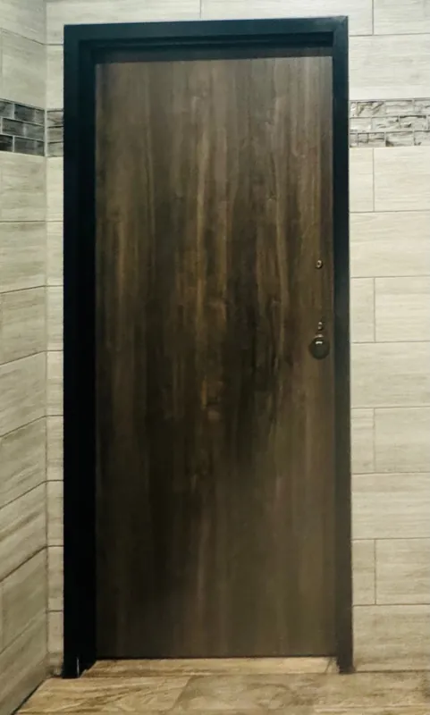 Dark woodgrain door in a black frame against white brick tile